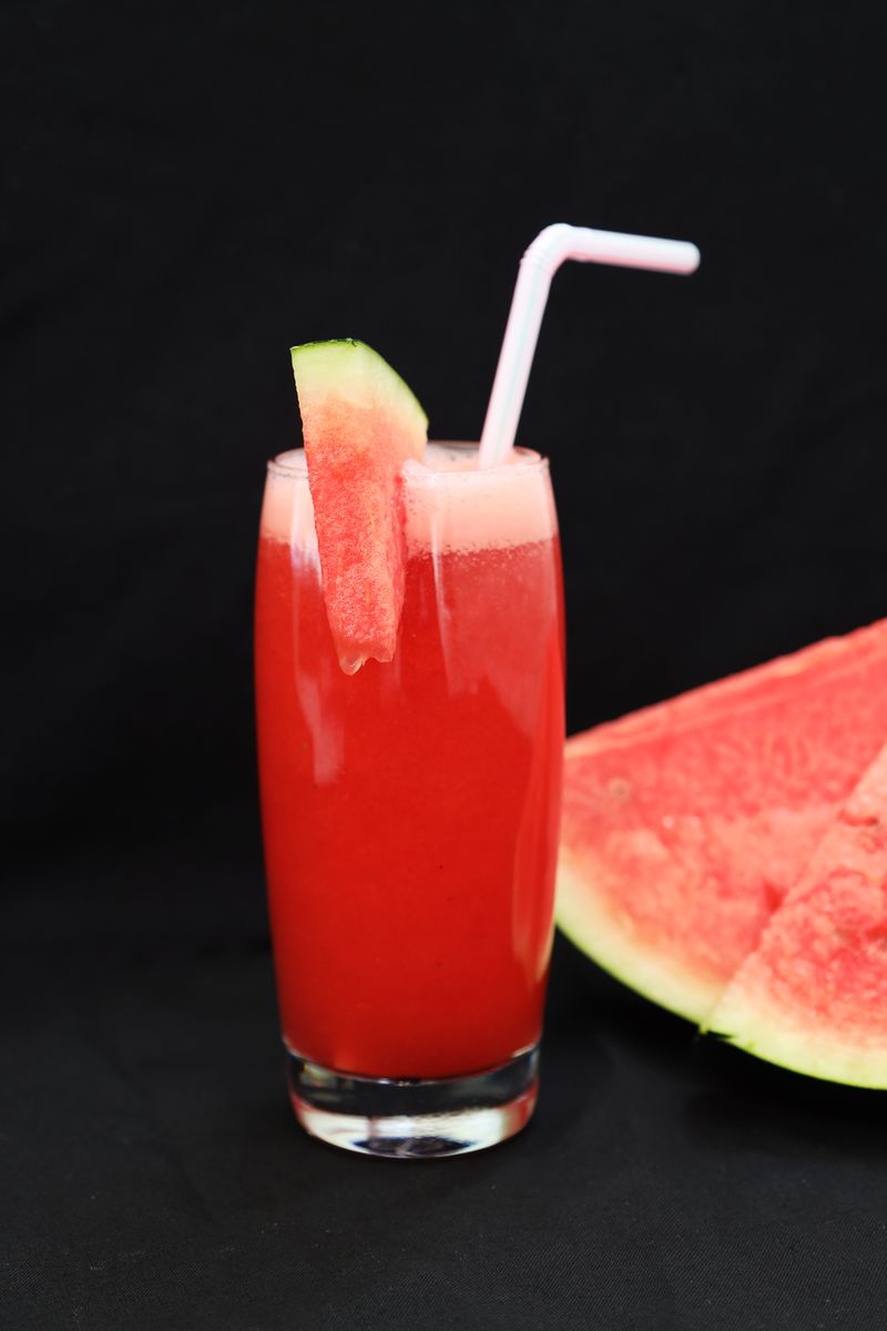 Bicchiere di succo d'anguria con cannuccia accanto a una fetta di anguria