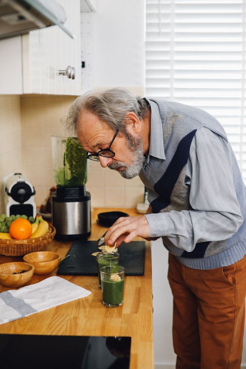 Uomo anziano che prepara un frullato verde nella sua cucina